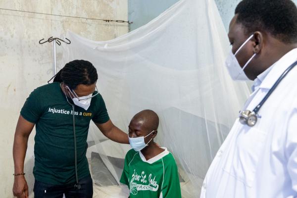 Dr. Maxo Luma, PIH Liberia Executive Director, and Dr. John Paul Otuba, PIH Liberia TB/HIV Lead, with Joe, a 24-year-old carpenter with MDR-TB, receive inpatient treatment at J.J. Dossen Memorial Hospital in Maryland County, Liberia. 
